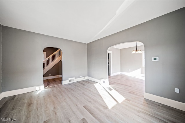 empty room with wood finished floors, visible vents, lofted ceiling, arched walkways, and a notable chandelier