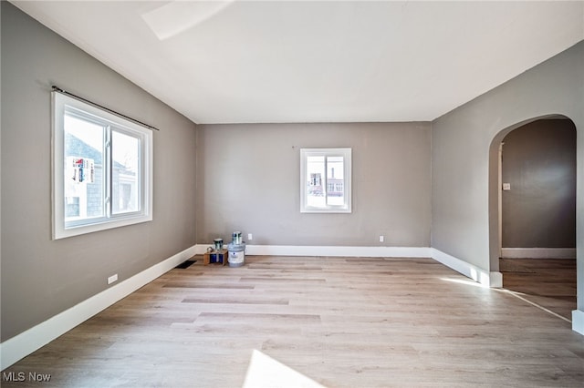 empty room with arched walkways, baseboards, and wood finished floors