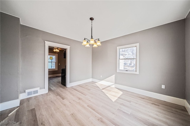 unfurnished room with baseboards, wood finished floors, visible vents, and a chandelier