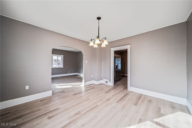 spare room with a notable chandelier, baseboards, arched walkways, and light wood finished floors