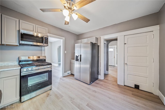 kitchen with stainless steel appliances, arched walkways, light wood-style floors, and light countertops