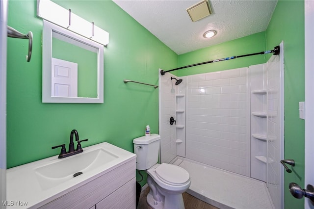 bathroom with vanity, a textured ceiling, visible vents, walk in shower, and toilet