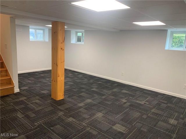 basement featuring dark carpet, stairs, baseboards, and a paneled ceiling