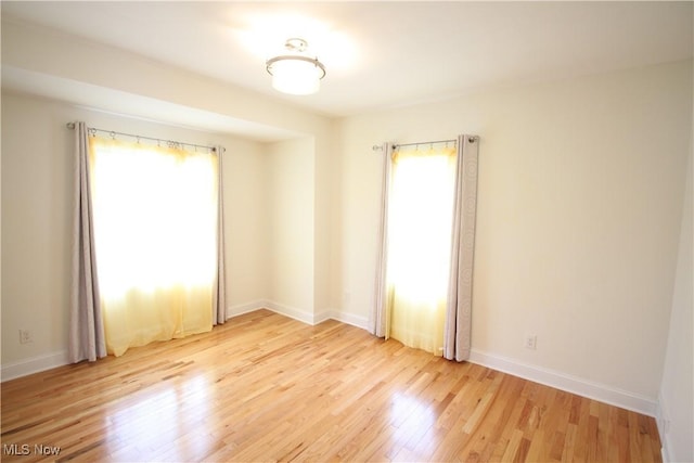 empty room with baseboards, a healthy amount of sunlight, and light wood-style flooring