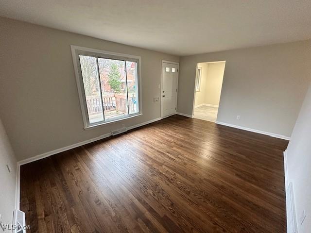 empty room with visible vents, baseboards, and dark wood-type flooring