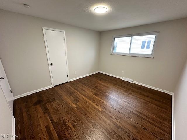 unfurnished bedroom with baseboards and dark wood-type flooring