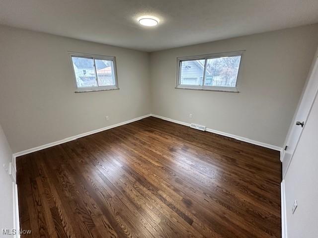 unfurnished bedroom featuring dark wood-style floors, visible vents, and baseboards