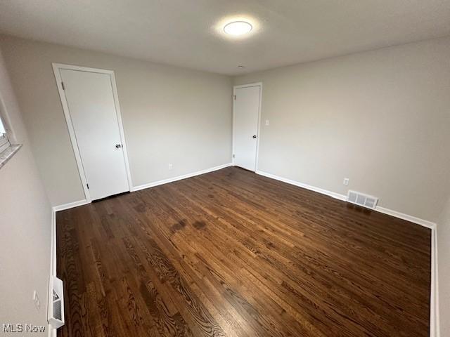 empty room featuring baseboards, visible vents, and dark wood-style flooring