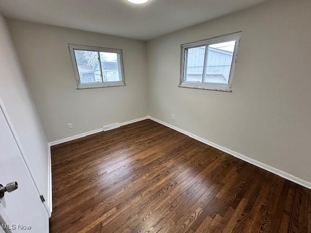 spare room featuring plenty of natural light, baseboards, and dark wood-style flooring