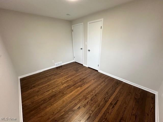 unfurnished room with dark wood-style floors, visible vents, and baseboards