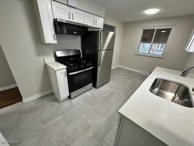 kitchen with a sink, freestanding refrigerator, white cabinets, light countertops, and gas range