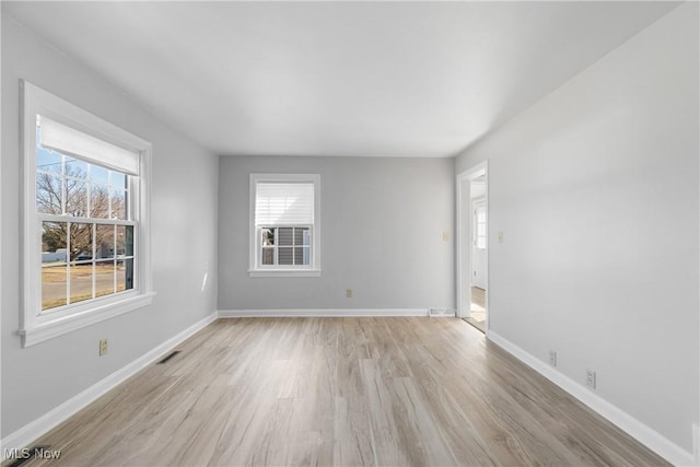 spare room featuring light wood finished floors, visible vents, and baseboards