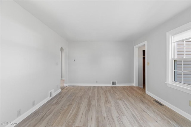 unfurnished room featuring light wood-style floors, arched walkways, visible vents, and baseboards