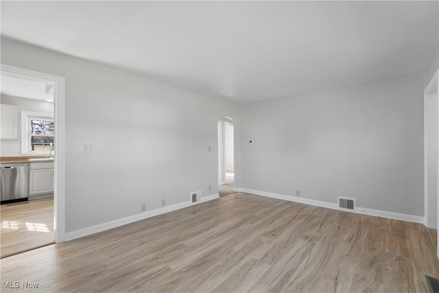 spare room with baseboards, light wood-type flooring, arched walkways, and visible vents