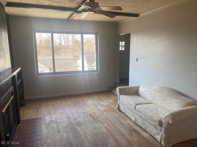 living area with a ceiling fan, beam ceiling, wood finished floors, and baseboards