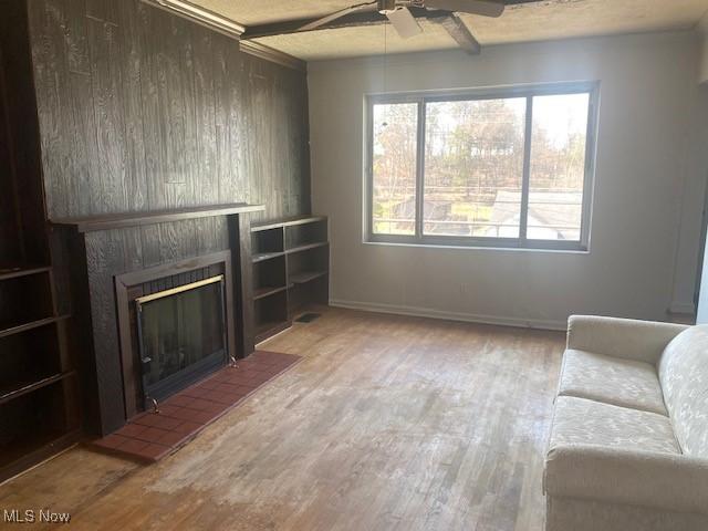 unfurnished living room with beam ceiling, wood finished floors, a ceiling fan, and a tiled fireplace