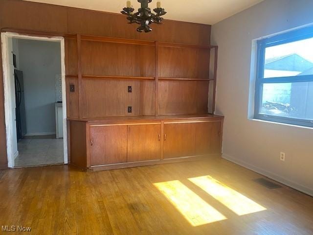 unfurnished dining area featuring an inviting chandelier, wood finished floors, baseboards, and visible vents