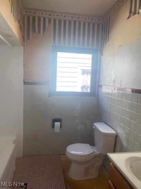 full bathroom with vanity, a wainscoted wall, wallpapered walls, tile walls, and toilet