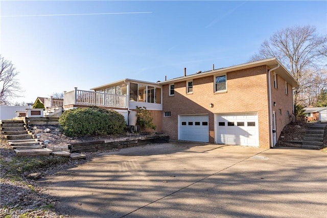 view of home's exterior featuring driveway, stairway, an attached garage, a sunroom, and brick siding