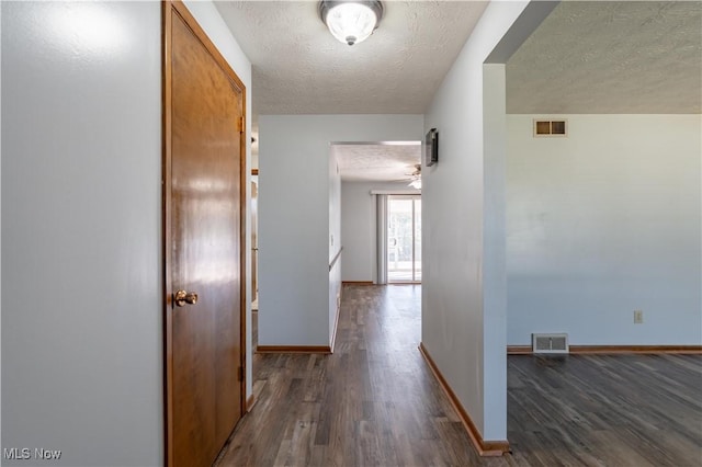 hall featuring dark wood finished floors, visible vents, and a textured ceiling