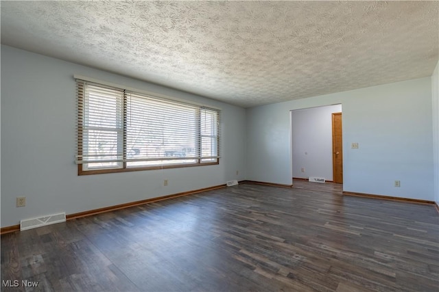 unfurnished room with a textured ceiling, wood finished floors, visible vents, and baseboards