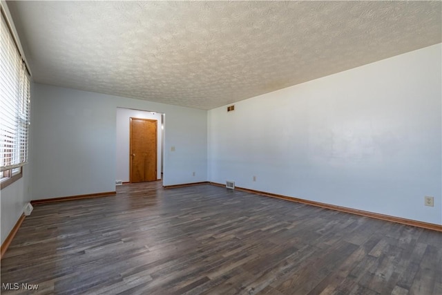 unfurnished room with visible vents, baseboards, dark wood-type flooring, and a textured ceiling