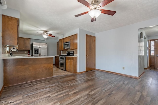 kitchen with baseboards, ceiling fan, wood finished floors, brown cabinetry, and stainless steel appliances