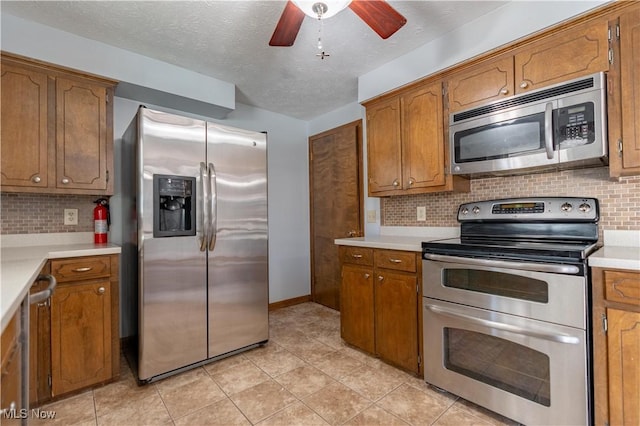 kitchen with brown cabinets, appliances with stainless steel finishes, ceiling fan, and light countertops