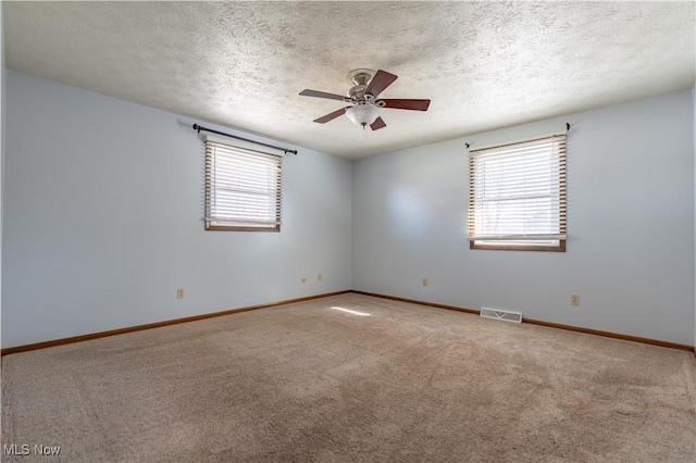 empty room featuring visible vents, plenty of natural light, carpet floors, and a ceiling fan