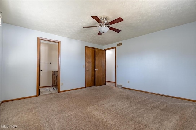 unfurnished bedroom with visible vents, baseboards, ensuite bath, a textured ceiling, and light carpet