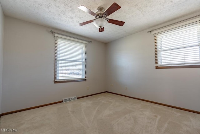 spare room featuring a textured ceiling, plenty of natural light, visible vents, and light carpet