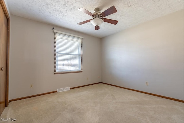 empty room with visible vents, baseboards, light carpet, a textured ceiling, and a ceiling fan