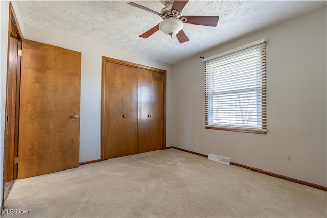 unfurnished bedroom featuring visible vents, baseboards, light carpet, a closet, and a textured ceiling