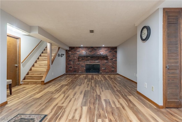 unfurnished living room featuring wood finished floors, visible vents, baseboards, stairs, and a brick fireplace