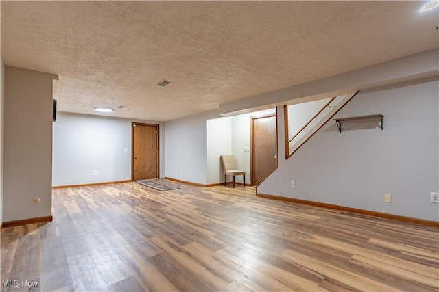 finished below grade area with visible vents, baseboards, a textured ceiling, and wood finished floors