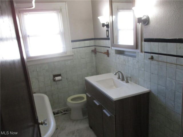 full bathroom with tile walls, toilet, a healthy amount of sunlight, and vanity