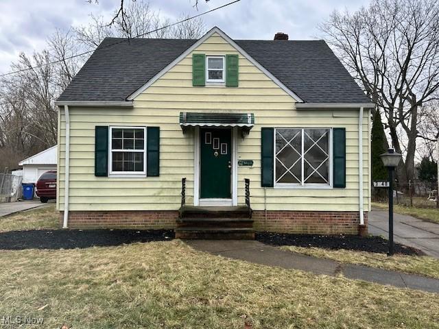 bungalow-style house with a shingled roof, entry steps, a front yard, a chimney, and a garage