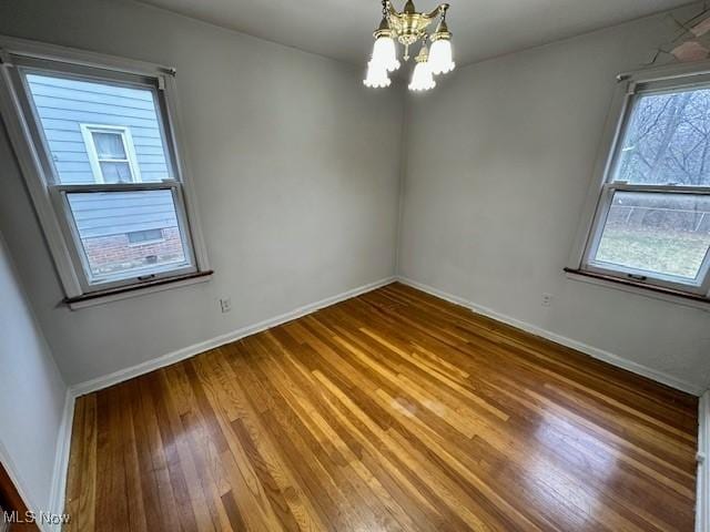 empty room featuring baseboards, a notable chandelier, and wood finished floors