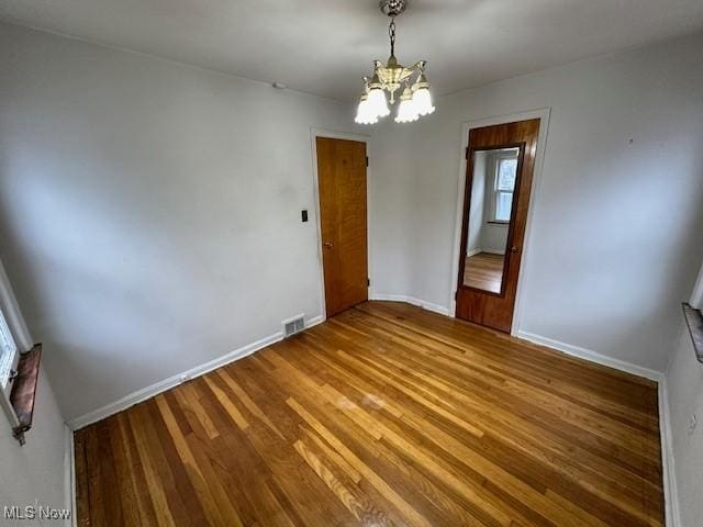 empty room featuring visible vents, wood finished floors, baseboards, and a chandelier