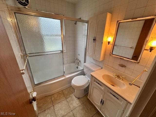 full bathroom with tile patterned flooring, bath / shower combo with glass door, toilet, vanity, and tile walls