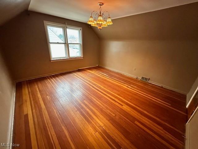 additional living space featuring visible vents, lofted ceiling, an inviting chandelier, and hardwood / wood-style floors