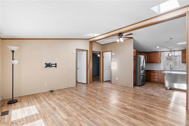 unfurnished living room featuring vaulted ceiling with skylight, light wood-style floors, a ceiling fan, and a textured ceiling