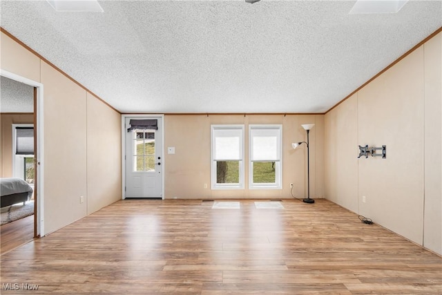 unfurnished living room with a textured ceiling, wood finished floors, and ornamental molding