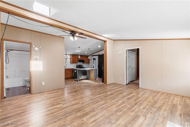 unfurnished living room featuring vaulted ceiling with skylight, light wood finished floors, and ceiling fan