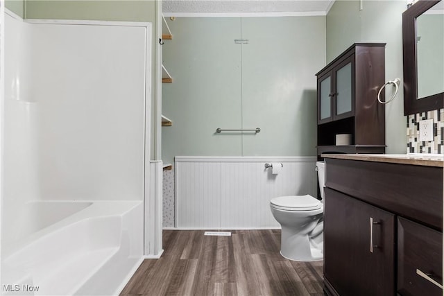 bathroom featuring toilet, ornamental molding, wainscoting, wood finished floors, and vanity