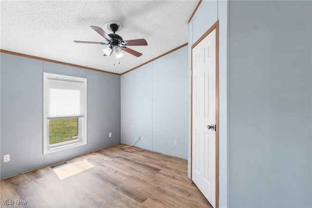 unfurnished bedroom featuring visible vents, ornamental molding, a textured ceiling, wood finished floors, and ceiling fan