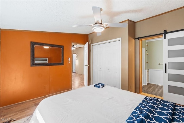 bedroom with ceiling fan, a barn door, wood finished floors, a closet, and a textured ceiling