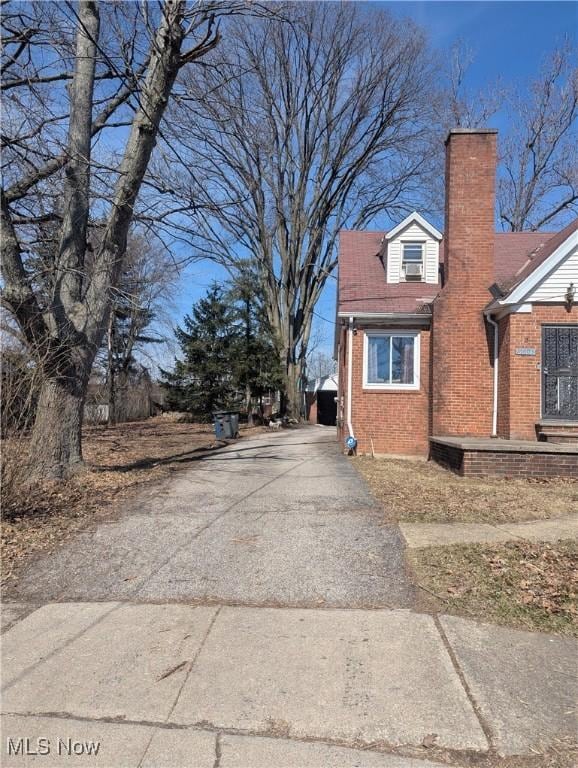 view of side of property featuring aphalt driveway, brick siding, and a chimney