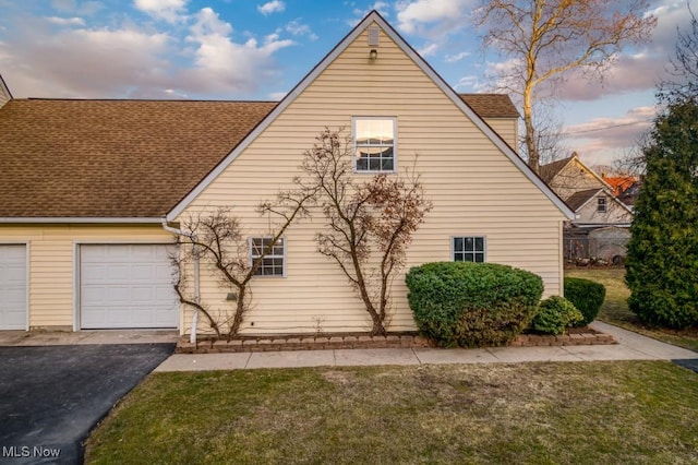 view of side of home with a garage, a lawn, a shingled roof, and aphalt driveway