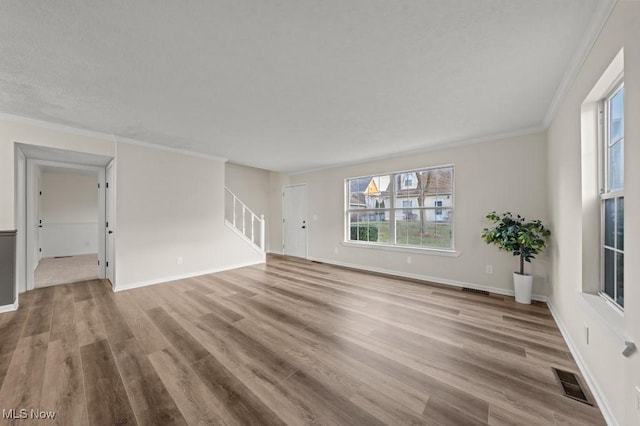 unfurnished living room featuring visible vents, wood finished floors, crown molding, baseboards, and stairs